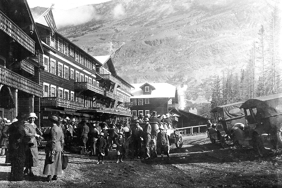 Many Glacier Hotel with groups of tourists waiting to board the old White touring buses, circa 1920. Courtesy Glacier National Park.