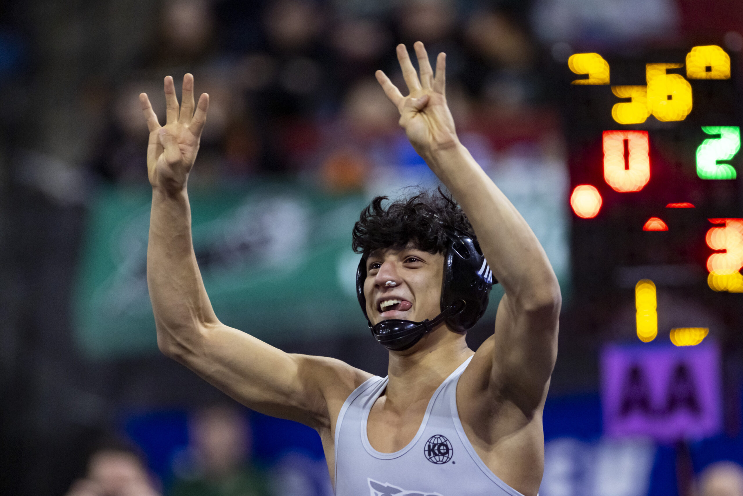 A profile shot of a wrestler from Glacier High School holding both hands above his head with four fingers outstretched, indicating his fourth state title.